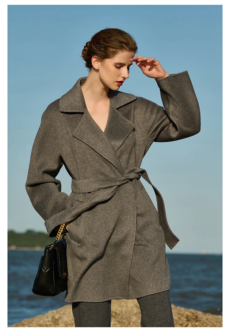 Model wearing a Sandstone wrap cashmere coat, shielding her eyes from sunlight. From Borcelleclothes.