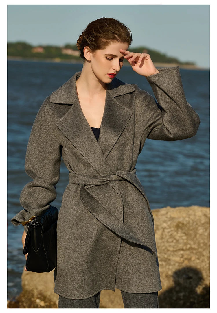 Model wearing a Sandstone wrap cashmere coat, touching her forehead. From Borcelleclothes.