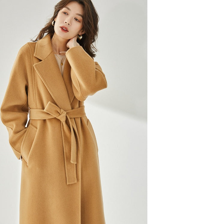 A model wearing the Women's Wrap Coat Redefined in Brown Sugar, touching her neck, highlighting the coat’s sophisticated drape and effortless wearability. From Borcelleclothes.