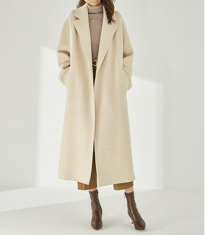 A model wearing the Women's Wrap Coat Redefined in Soft Amber, hands in pockets, captured from the foot side, highlighting its sculptural mid-calf length. From Borcelleclothes.