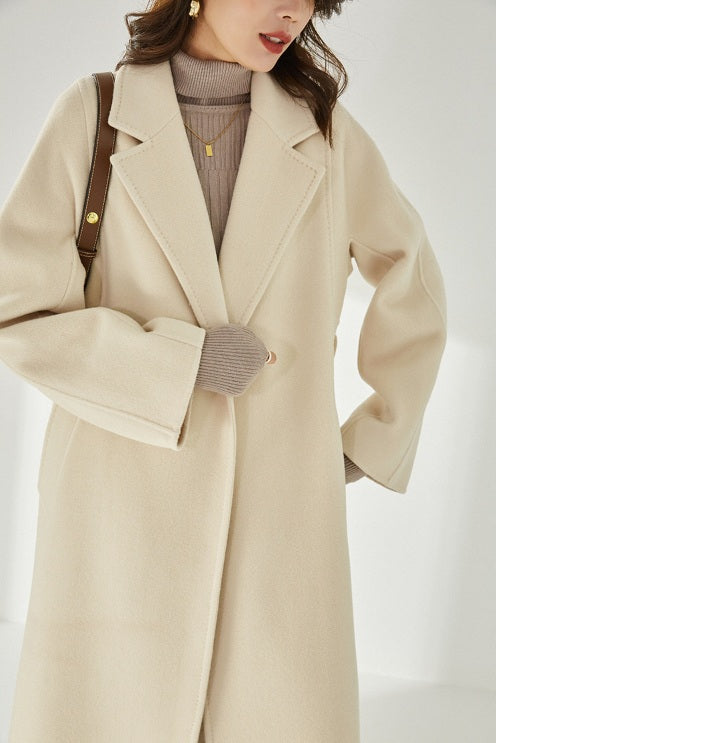 A model wearing the Women's Wrap Coat Redefined in Soft Amber, holding the lapels together, showcasing its structured yet fluid design. From Borcelleclothes.