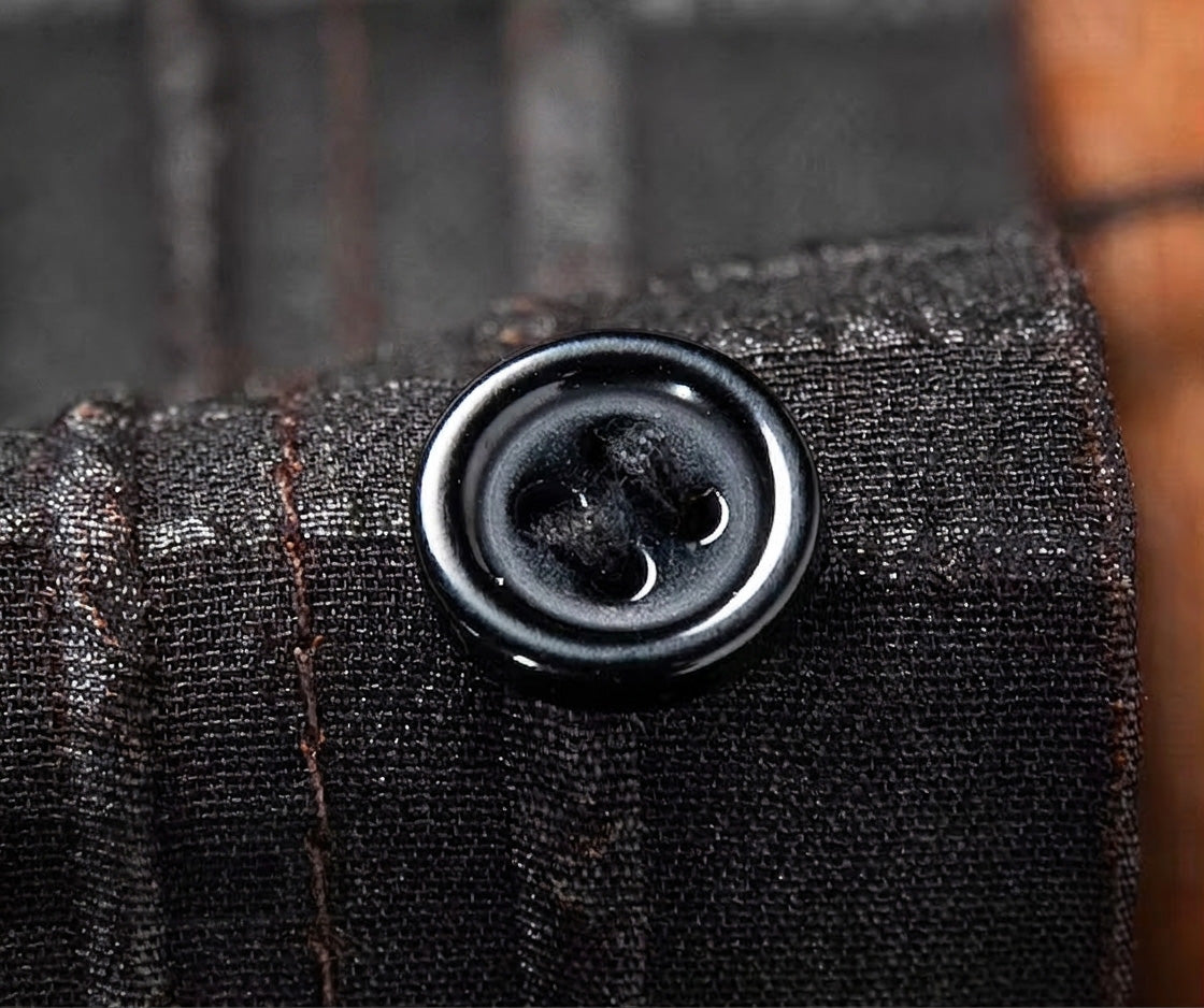 Macro shot of a neat black button sewn onto the textured placket of a Checked Nocturne silk shirt — From Borcelleclothes.
