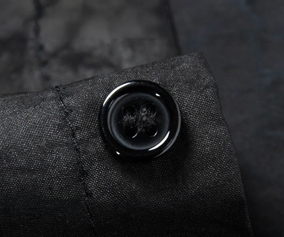 A focused macro shot of the deep, high-gloss black button contrasting sharply against the matte, mineral surface of the Obsidian Jaguar silk shirt placket — From Borcelleclothes.