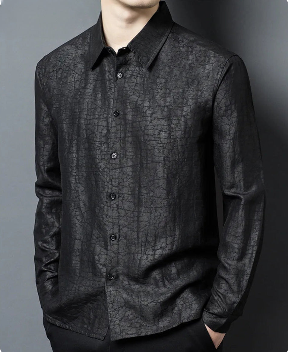 A man with his hands in his trousers pockets, showcasing the soft drape and clean lines of the Men's Gambiered Guangdong Silk Shirt in Obsidian Jaguar, reflecting an air of quiet confidence — From Borcelleclothes.