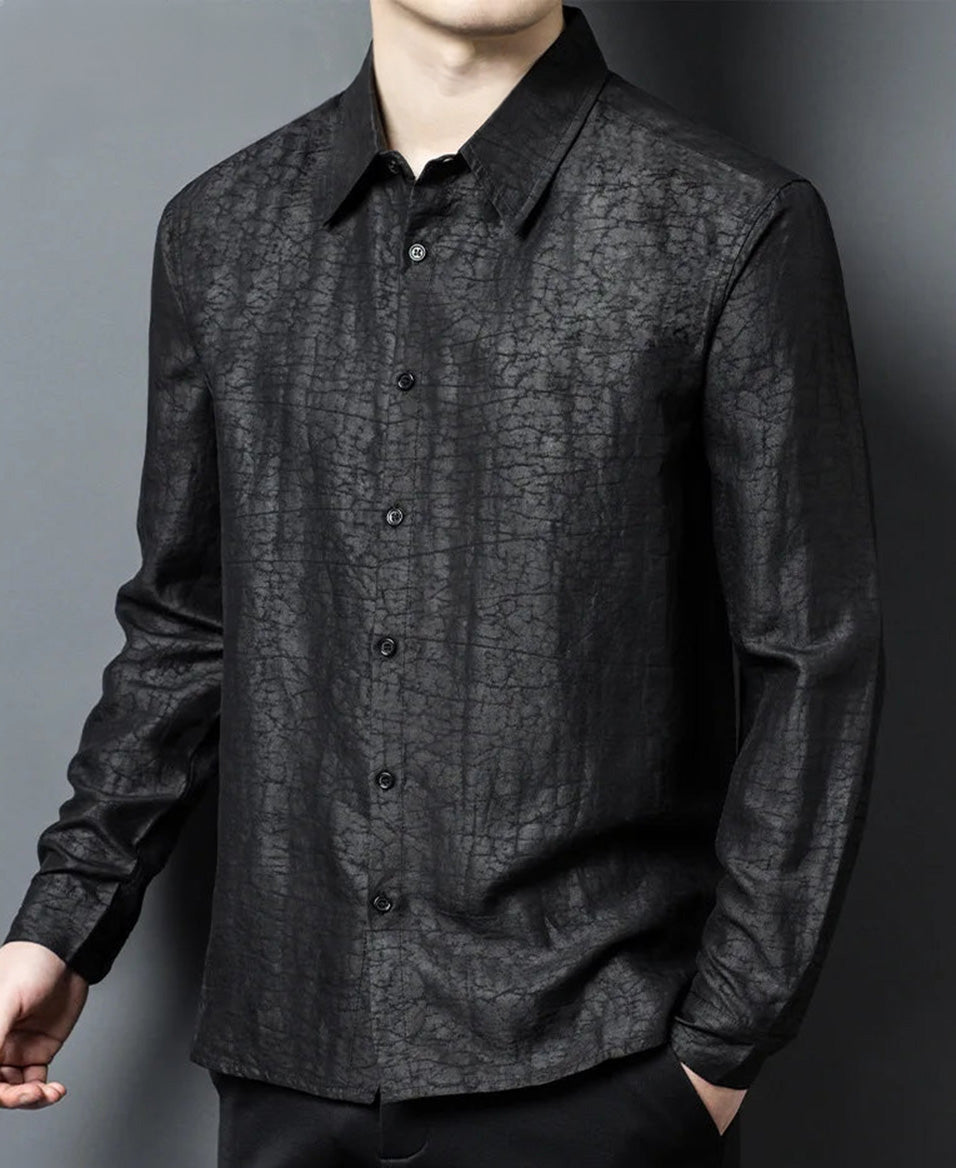 A side profile of a man standing with intimidating composure, capturing how the light plays on the predatory undertones and subtle fractures of the matte Obsidian Jaguar silk shirt — From Borcelleclothes.