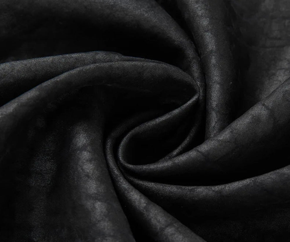 Macro shot of the authentic Xiangyunsha silk in Obsidian Jaguar, folded into a tight spiral to highlight its unique matte-graphite relief, organic texture, and natural craquelure — From Borcelleclothes.