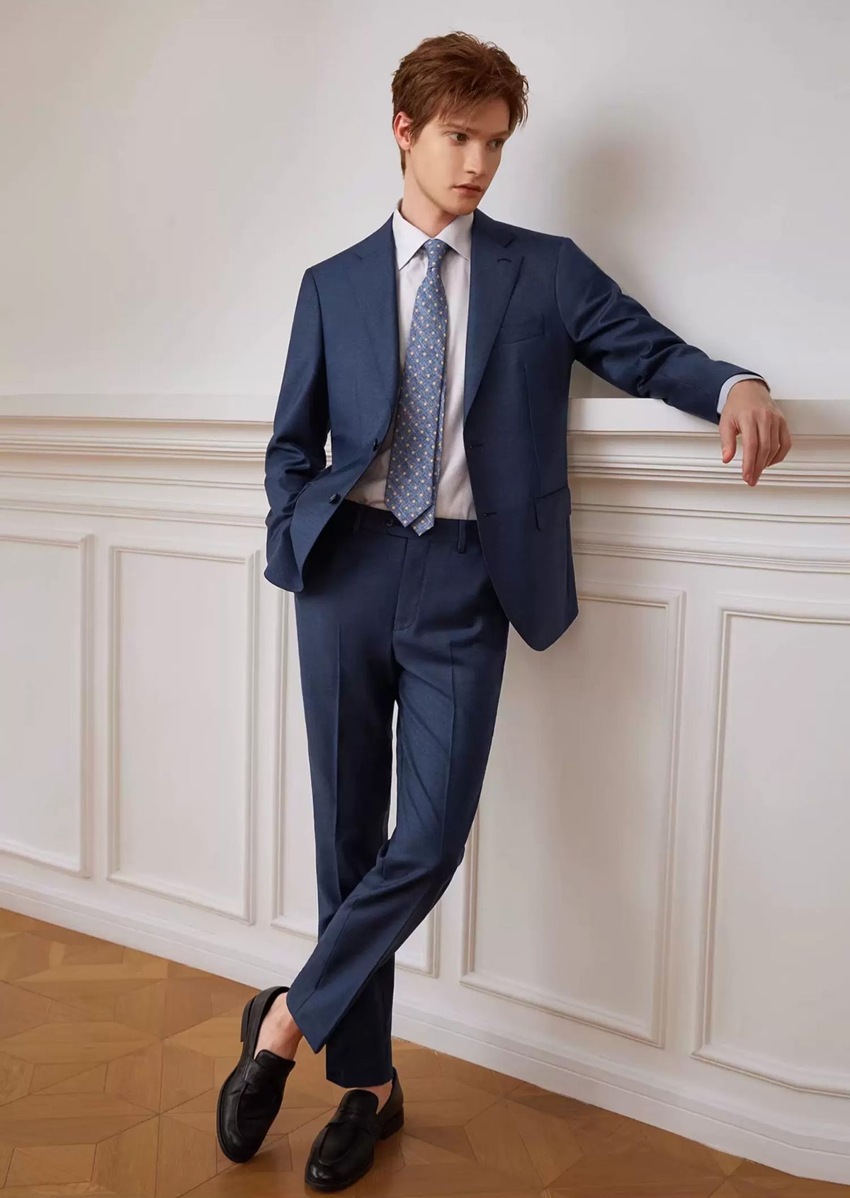 Full-length view of a model in the Salt Wave melange wool suit leaning against a wall with crossed legs — From Borcelleclothes.