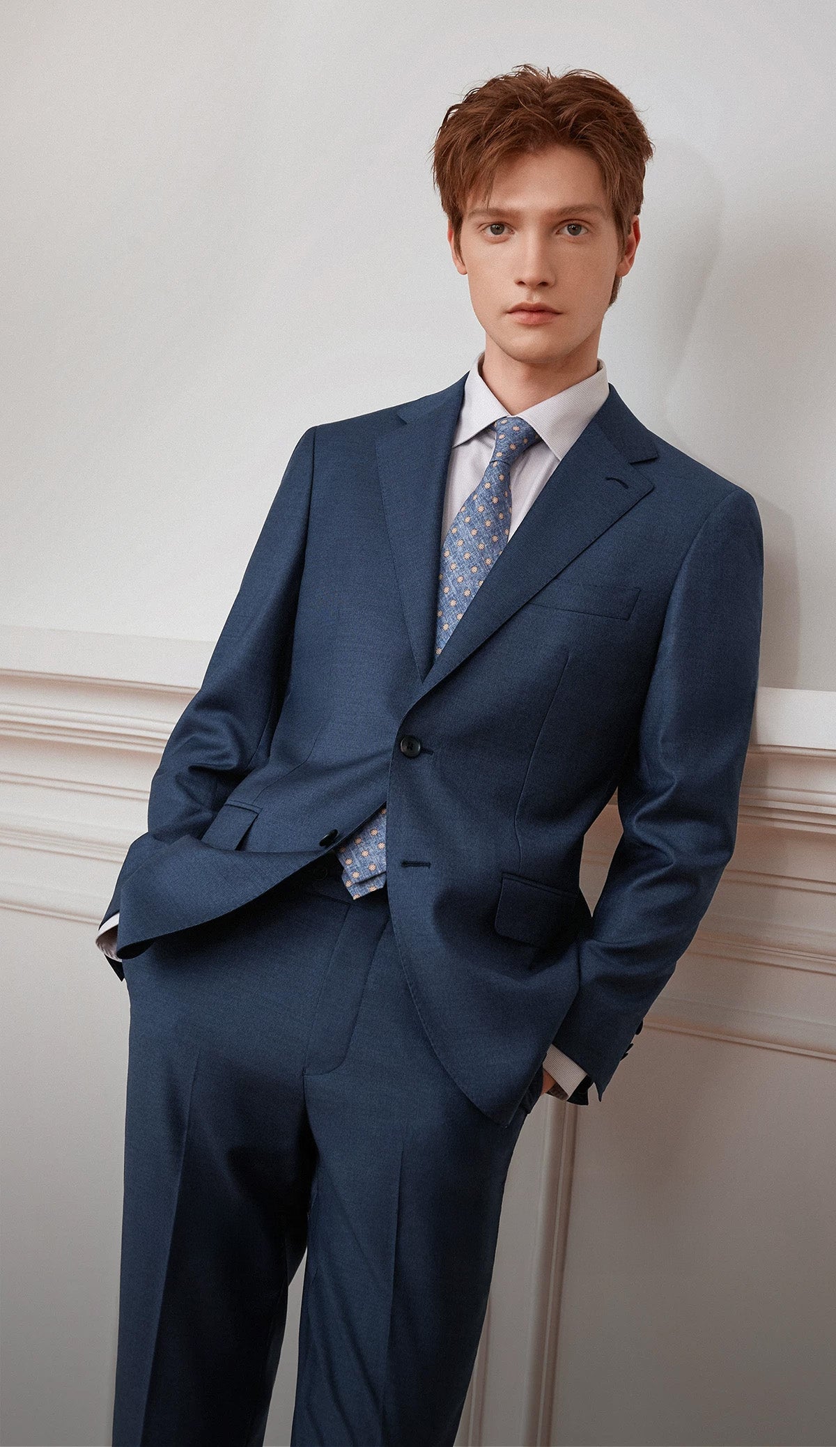 Male model in a tailored Salt Wave blue-gray melange wool suit leaning against a wall — From Borcelleclothes.