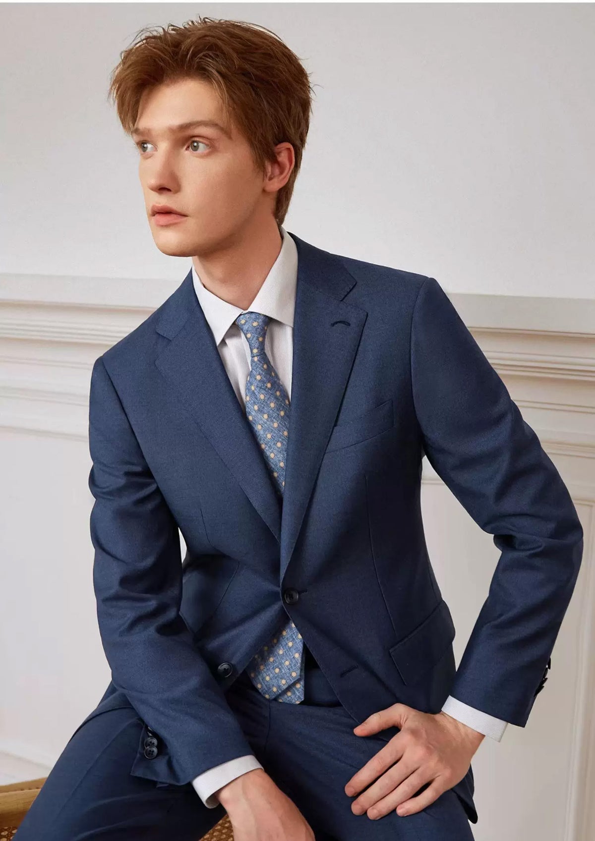 Model perched on the back of a chair looking to the side in the tailored Salt Wave melange wool suit — From Borcelleclothes.