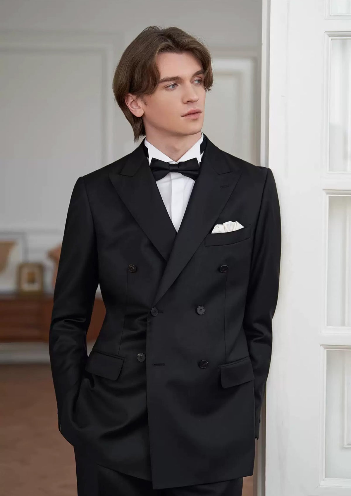 Cinematic shot of the model leaning against a doorway in a black double-breasted suit, reflecting quiet tension and anticipation — From Borcelleclothes.
