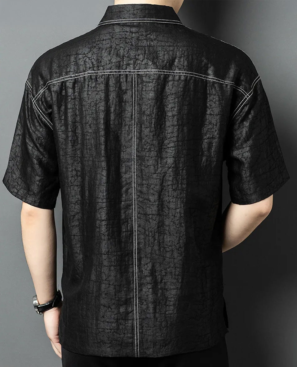 Back view of a man wearing the black silk polo shirt, featuring the distinctive decorative white contrast topstitching on the upper back and a central double topstitching — From Borcelleclothes.