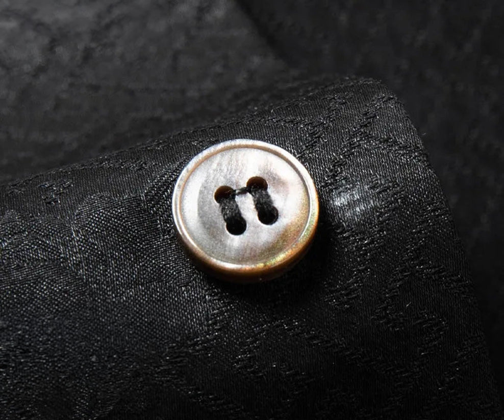 Macro shot of the premium black mother-of-pearl (MOP) button on the Beyond Mistletoe silk overshirt, showcasing its natural iridescent luster, neat stitching, and minimalist high-end finish. — From Borcelleclothes.