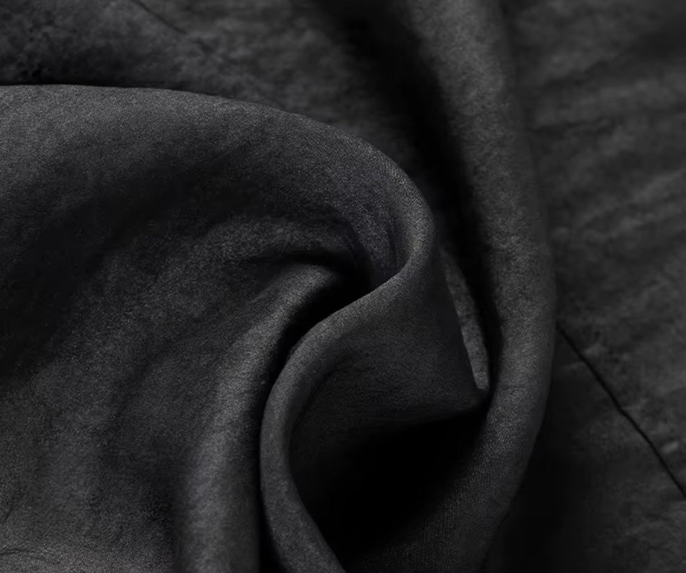 Studio close-up of the matte Parchment Graphite Xiangyunsha silk fabric, elegantly folded in a spiral to display its deep texture and substantial drape — From Borcelleclothes.