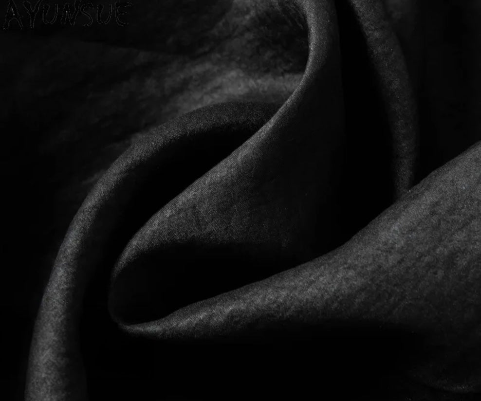 Macro view of the wave-folded texture of authentic black Xiangyunsha silk, displaying its unique, living matte patina. From Borcelleclothes.
