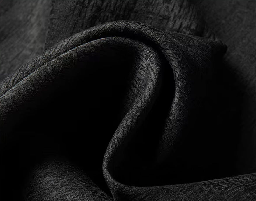 Close-up of the heavyweight double-weave silk fabric folded into deep waves, displaying the contrast between the semi-gloss graphite base and the matte, elephant-skin textured relief - From Borcelleclothes.