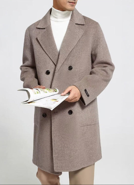 A model wearing the Men’s 900g Wool Coat in Warm Grey, holding a journal, highlighting the coat’s relaxed yet refined silhouette. From Borcelleclothes.