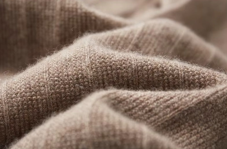 Men's Cashmere V-Neck Sweater in Sandrift slightly being held to highlight its soft, lightweight cashmere material and textured front. From Borcelleclothes.