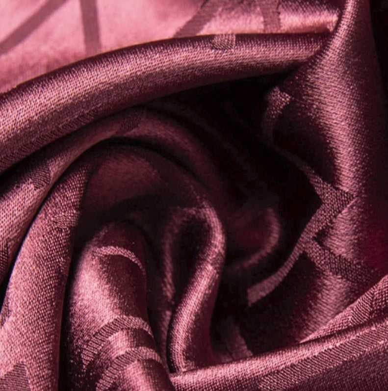 Coral Tree Mulberry silk fabric folded in a spiral, revealing its warm-toned sheen and the inscribed jacquard pattern woven into the surface. From Borcelleclothes.