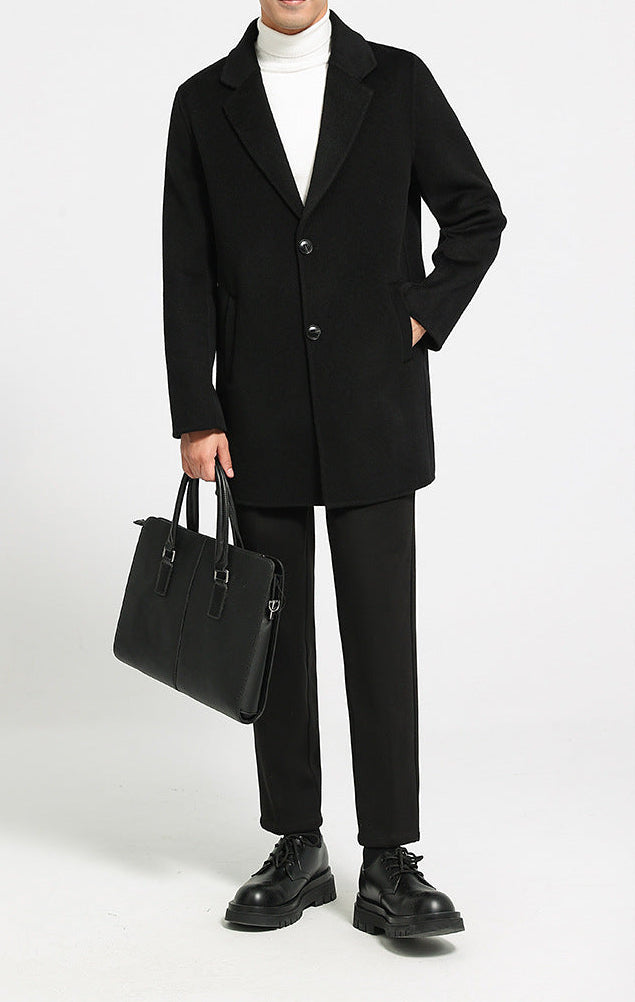Model holding a bag while wearing Men’s mid-length double-faced wool coat in Onyx with notch lapels and two-button closure. From Borcelleclothes.