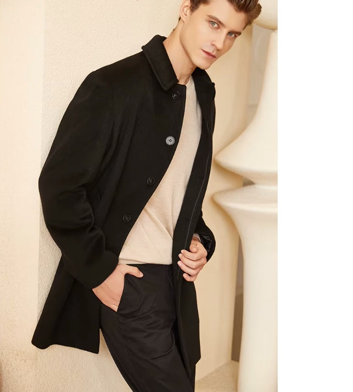 Model wearing the Men’s Minimalist Cashmere Coat in Zeus, standing near a decorative column, emphasizing the commanding presence of the deep near-black shade. From Borcelleclothes.