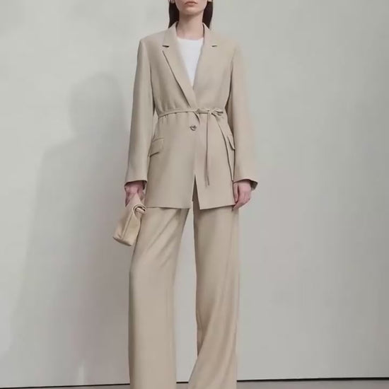 Video showcasing a Women’s crinkled viscose blazer in Soft Amber, Morning Blue, and Onyx colors, with deep textured folds, notch lapels, flap pockets, sculptural triangular button, and belt threaded through side openings. From Borcelleclothes.