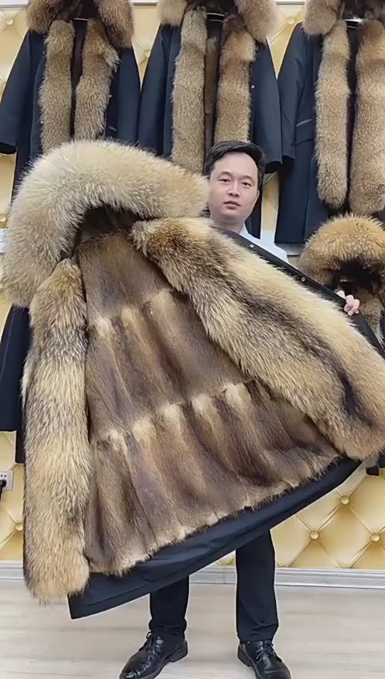 Video showcasing a Men’s mid-calf coat in River Bed color featuring detachable muskrat fur lining, voluminous raccoon hood, front patch pockets, and subtle rubberized details. From Borcelleclothes.