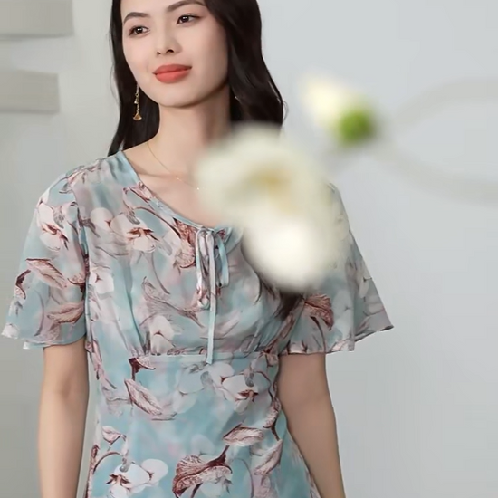 Video showcasing a Women's flared 100% crepe de chine silk dress in Celestial Bauhinia color. Featuring a front empire waist, delicate flutter sleeves, and wave-curved bottom flounces. — From Borcelleclothes.