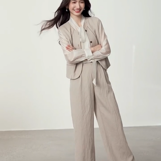 Video showcasing a Women's three-piece suit made of textured chocolate truffle viscose, featuring a deep round neckline vest with wave-stitch embroidery, straight-leg pleated trousers, and a lightweight semi-sheer blouse in elderflower shade with a transformable bow-tie collar. — From Borcelleclothes.