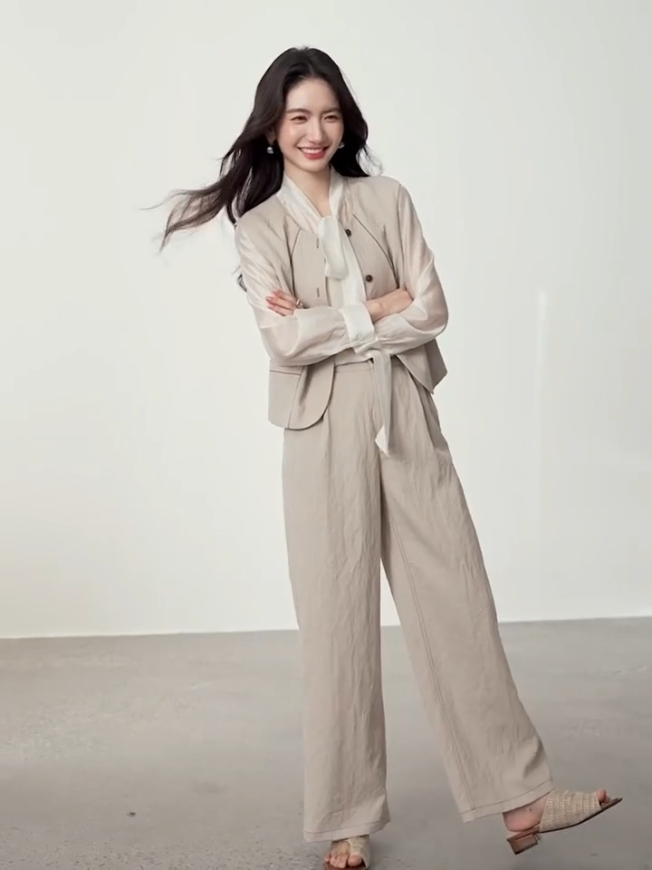 Video showcasing a Women's three-piece suit made of textured chocolate truffle viscose, featuring a deep round neckline vest with wave-stitch embroidery, straight-leg pleated trousers, and a lightweight semi-sheer blouse in elderflower shade with a transformable bow-tie collar. — From Borcelleclothes.