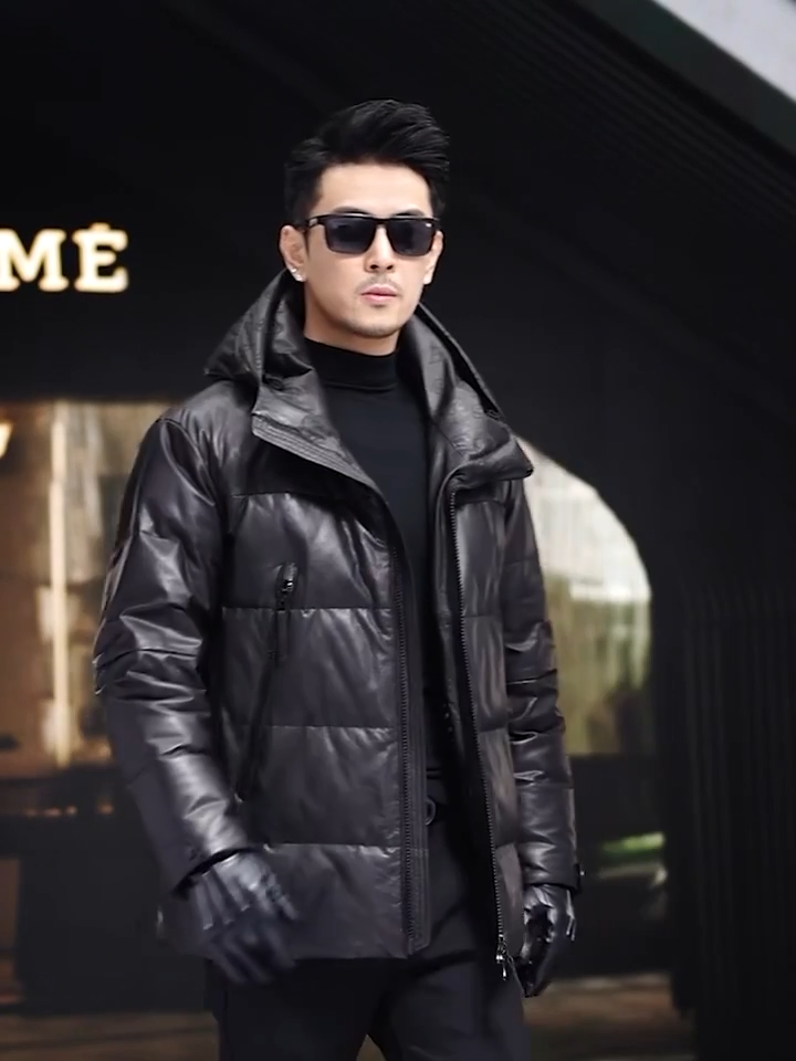 Video showcasing a Men’s sheepskin down jacket in Onyx with large diagonally zippered pockets, exposed central closure, sculptural hood, and tonal imprint under the collar — From Borcelleclothes.