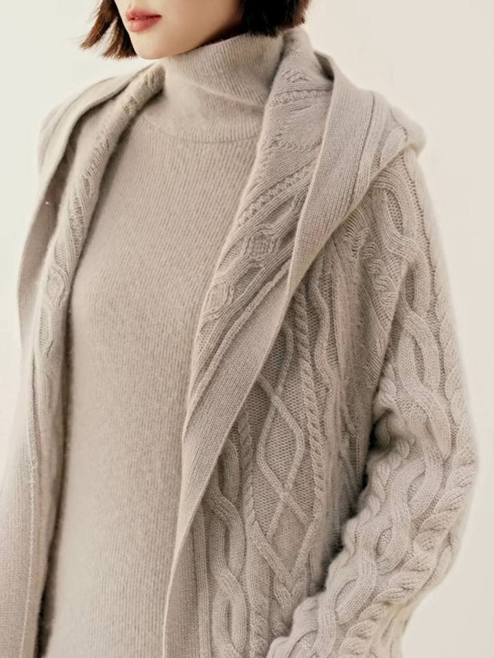 Video showcasing a Women's Luxurious Cable-Knit Cashmere Coat in Soft Amber and Pearl Bush, featuring intricate cable patterns, a loose-fitting silhouette, a wide ribbed bottom hem, large functional pockets, and an integrated hood for a timeless yet modern design, Borcelleclothes.