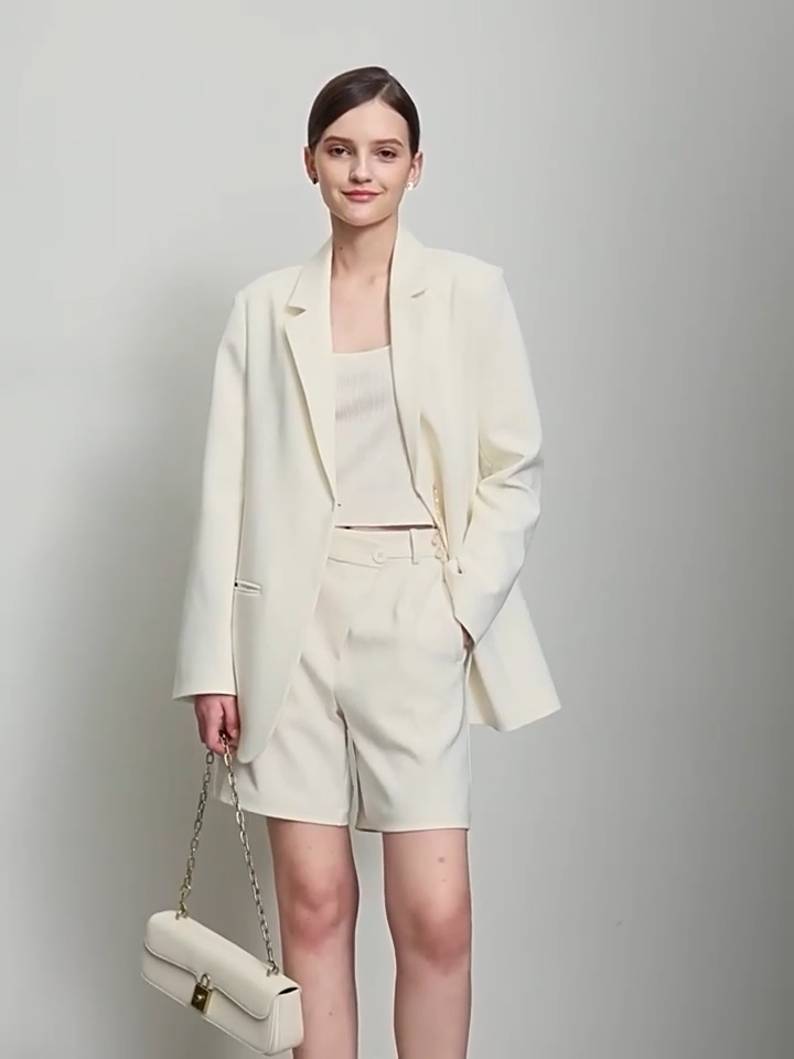 Video showcasing a Women’s wrap blazer in Pearl Bush, with hidden hook-and-eye closure, notch lapels, welt pockets, golden pendant accent, and thigh-length cut – From Borcelleclothes.