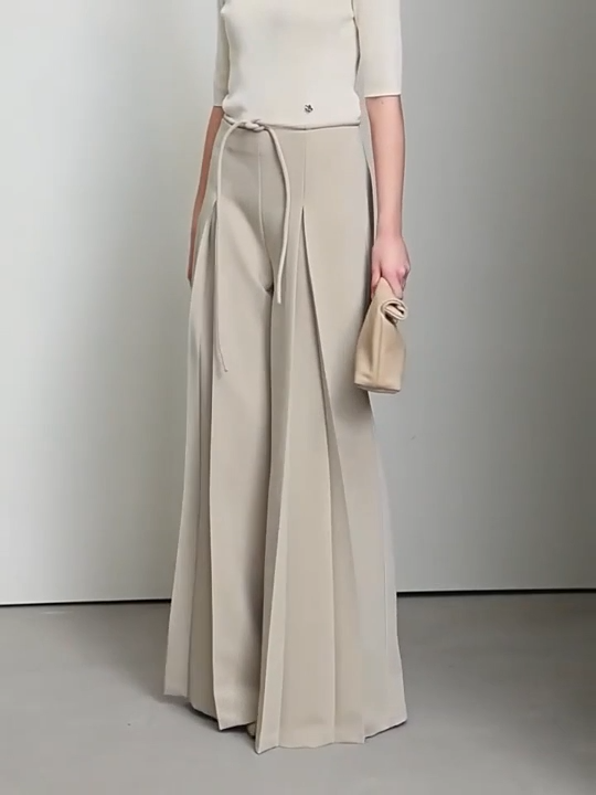 Video showcasing Women’s tailored draped trousers in Silk, featuring deep sculptural pleats and soft belt loops, styled with minimalist top and relaxed posture. From Borcelleclothes.