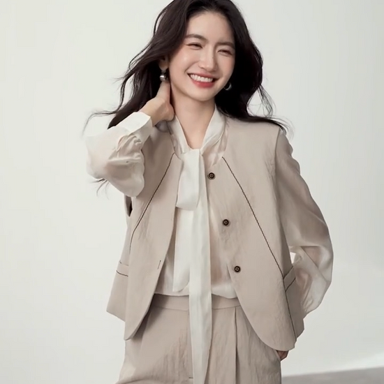 Video showcasing a Women's three-piece suit made of textured chocolate truffle viscose, featuring a deep round neckline vest with wave-stitch embroidery, straight-leg pleated trousers, and a lightweight semi-sheer blouse in elderflower shade with a transformable bow-tie collar. — From Borcelleclothes.
