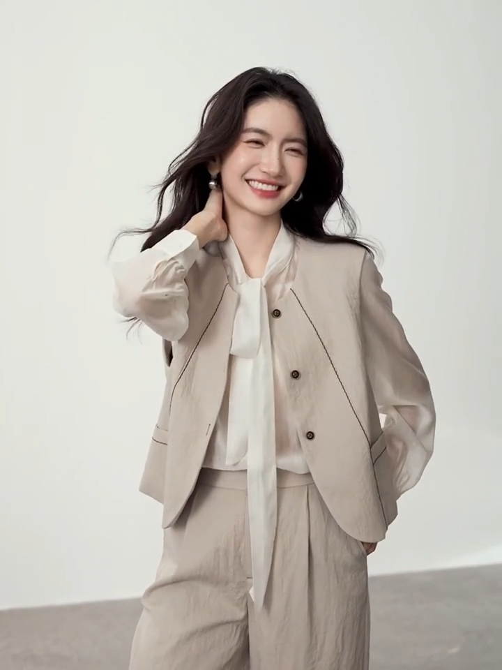 Video showcasing a Women's three-piece suit made of textured chocolate truffle viscose, featuring a deep round neckline vest with wave-stitch embroidery, straight-leg pleated trousers, and a lightweight semi-sheer blouse in elderflower shade with a transformable bow-tie collar. — From Borcelleclothes.