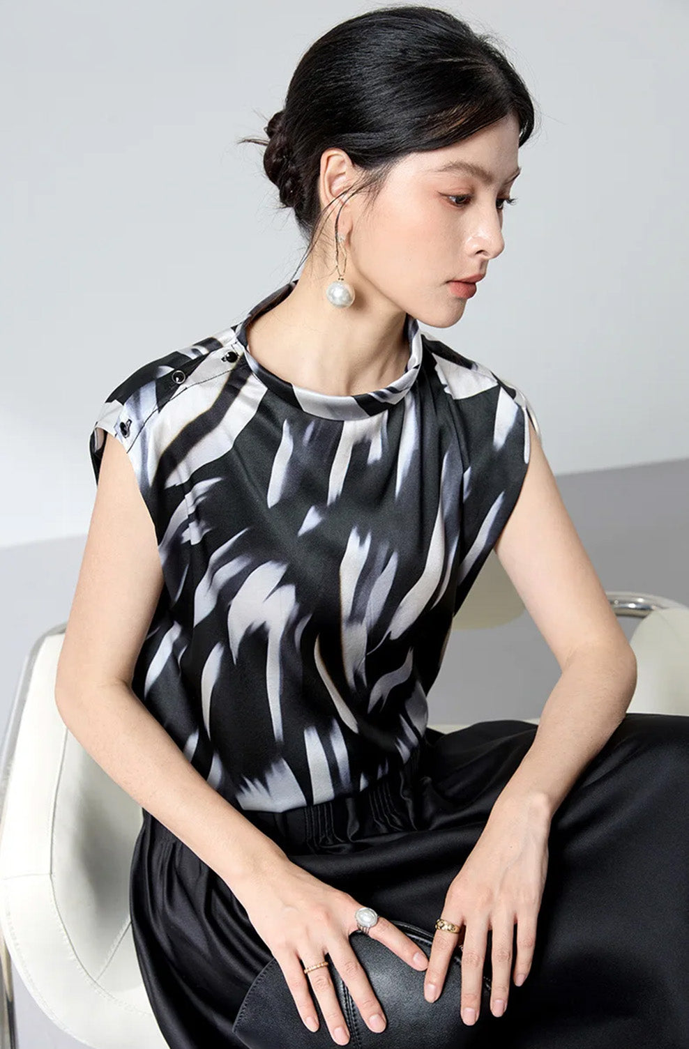 Seated model in Fleeting Impulse silk satin blouse holding an evening clutch — From Borcelleclothes.