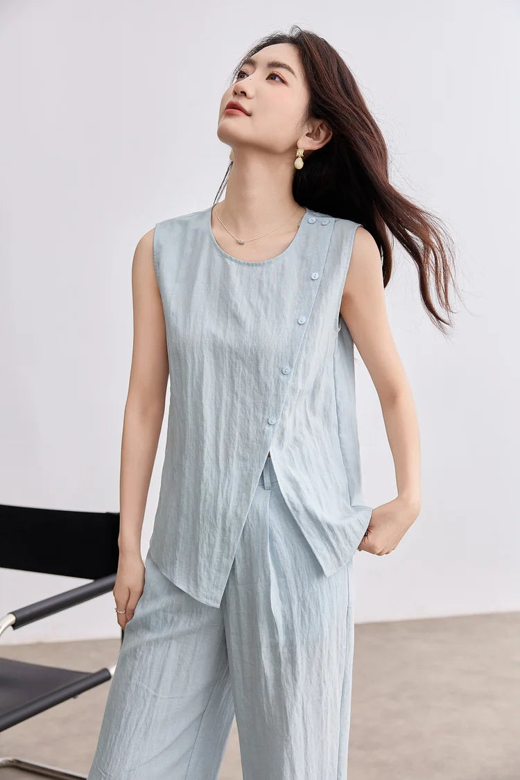A thoughtful woman looking up, wearing a light blue sleeveless asymmetrical top made of breathable Lyocell and linen — From Borcelleclothes.