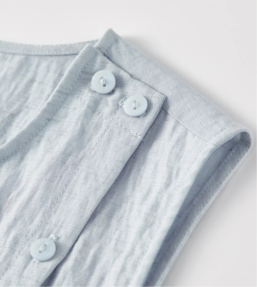 Detailed shot of the tonal buttons on the left shoulder of the asymmetrical wrap top — From Borcelleclothes.