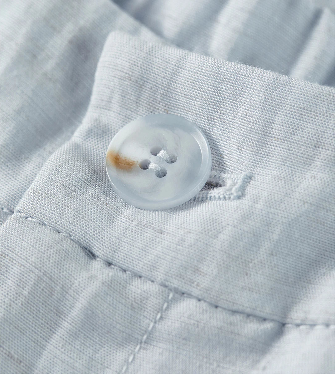 Macro view of the tonal button and clean waist finish of the pleated wide-leg trousers — From Borcelleclothes.