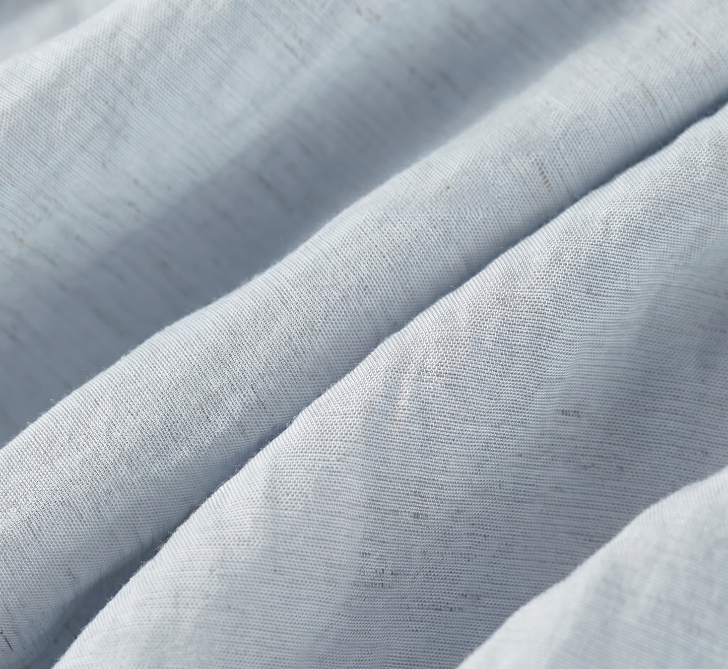 Close-up of the wave-folded crinkled fabric texture, showing the natural linen specks in a light blue Lyocell blend — From Borcelleclothes.