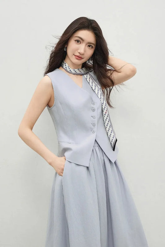 Woman wearing a lavender asymmetrical vest and midi skirt set, hand to hair — From Borcelleclothes.