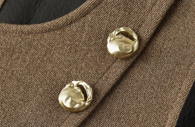 Macro shot of the two decorative gold-tone buttons on the asymmetrical wrap vest — From Borcelleclothes.