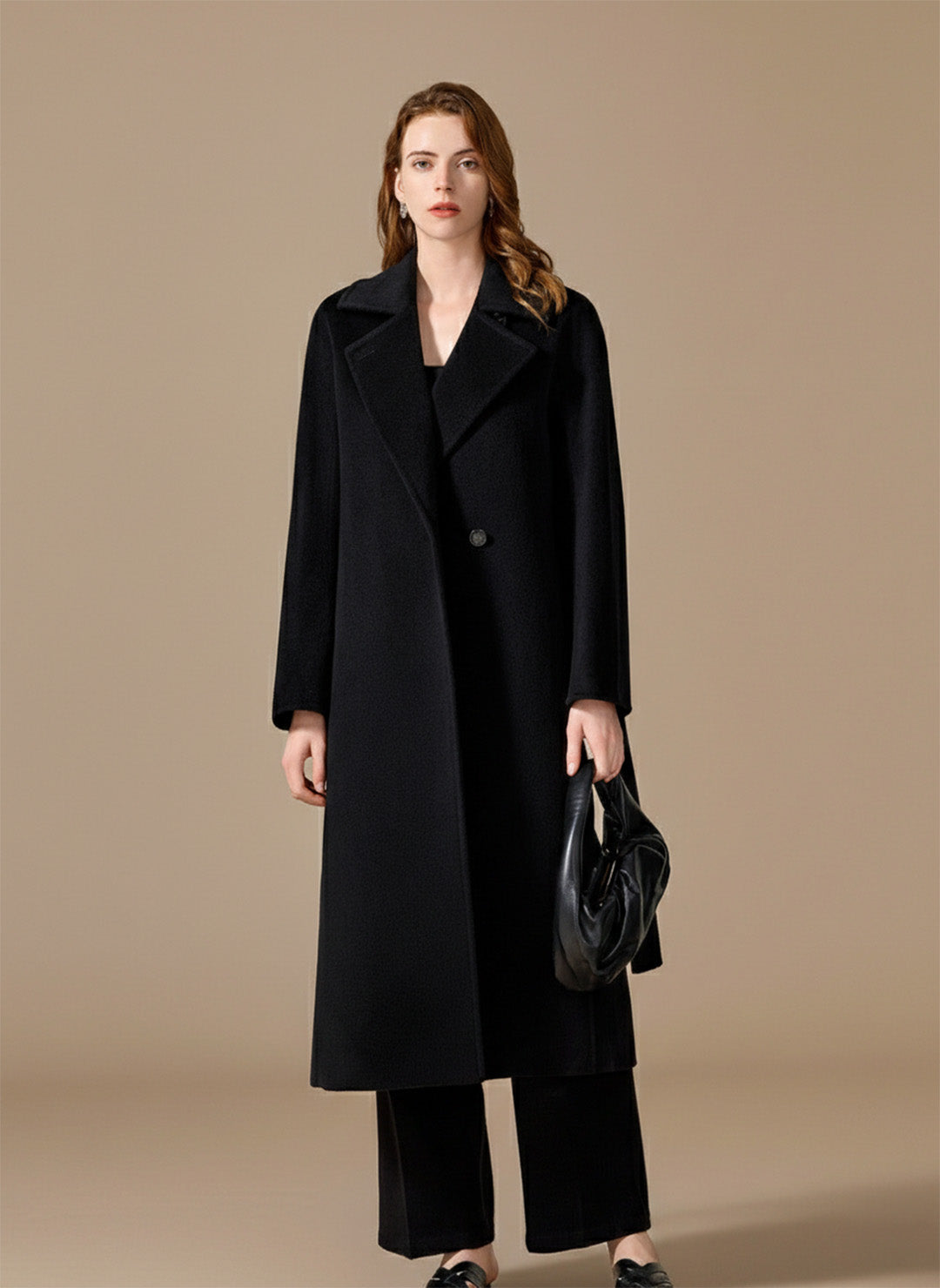 A woman wrapped in the Nightfall black Bactrian camel hair coat, holding a leather bag. From Borcelleclothes.