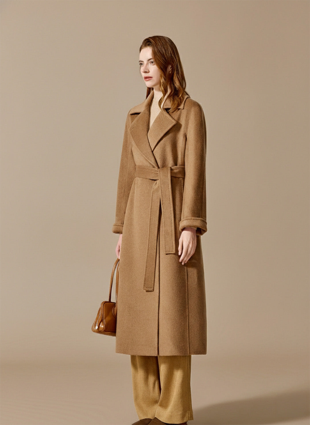 A woman in a Tumbleweed camel hair coat holding a matching bag, capturing a moment of serene, natural luxury. From Borcelleclothes.