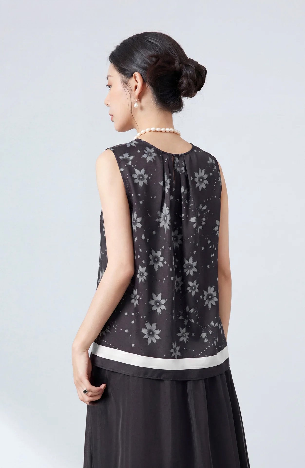 Rear view of a model wearing a sleeveless silk twill blouse showcasing the back pleats and border hem — From Borcelleclothes.