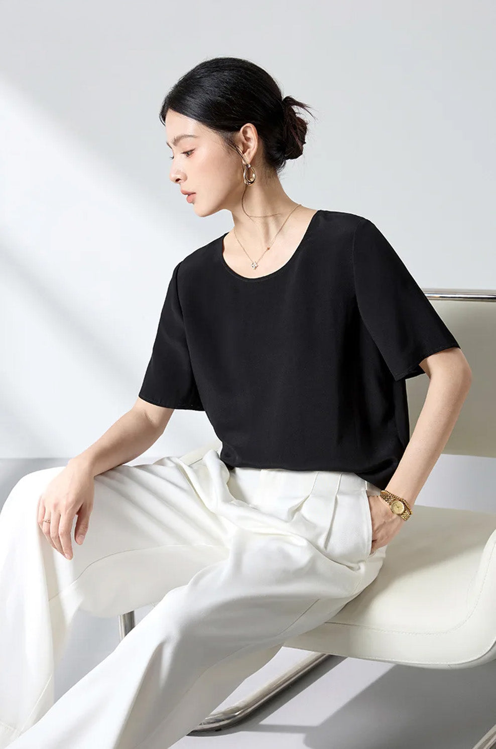 Model seated on a modern metal chair wearing the relaxed Calculated Canvas matte silk-viscose crepe top paired with white wide-leg trousers — From Borcelleclothes.