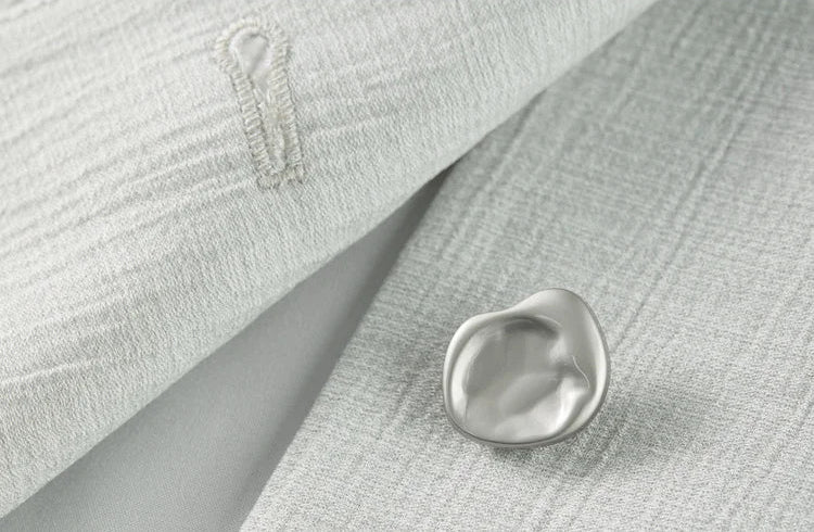 Macro shot of an unfastened ice-inspired embossed button on the textured viscose jacket. From Borcelleclothes.