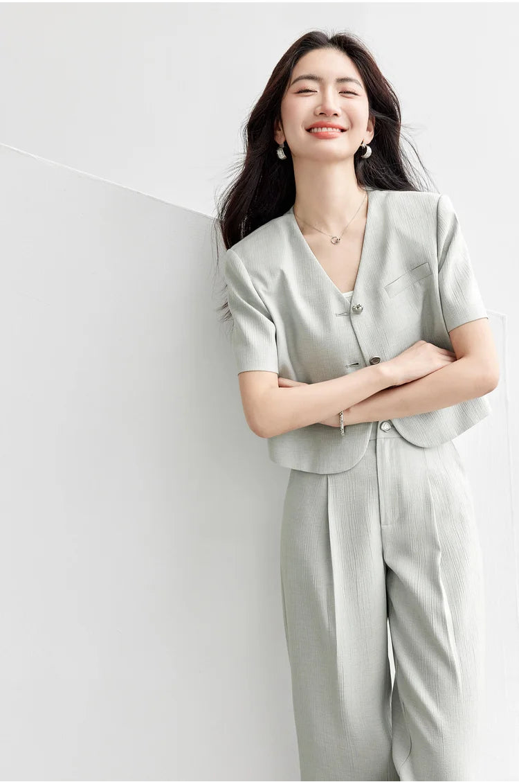 A woman with crossed arms in a sage-grey viscose jacket, highlighting the set-in short sleeves and structured shoulder design. From Borcelleclothes.