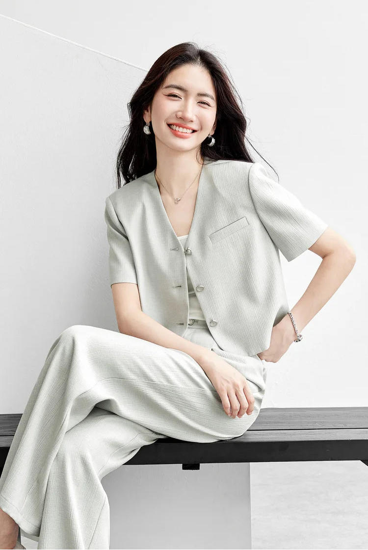 A woman sitting on a bench in a sage-grey wide-leg trousers set, demonstrating the relaxed yet sharp silhouette of the Named by Frost collection. From Borcelleclothes.