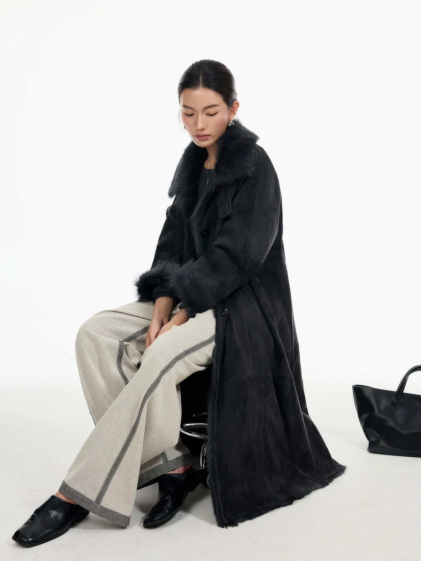 Model seated in a convertible collar goatskin coat in Tusch, with soft folds forming along the body and cuffs, revealing the quiet depth of the material — From Borcelleclothes.